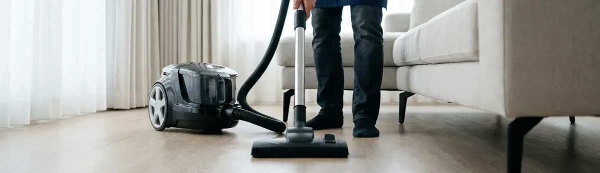 Professional house cleaner vacuuming a living room floor with a canister vacuum cleaner, Madison, WI.