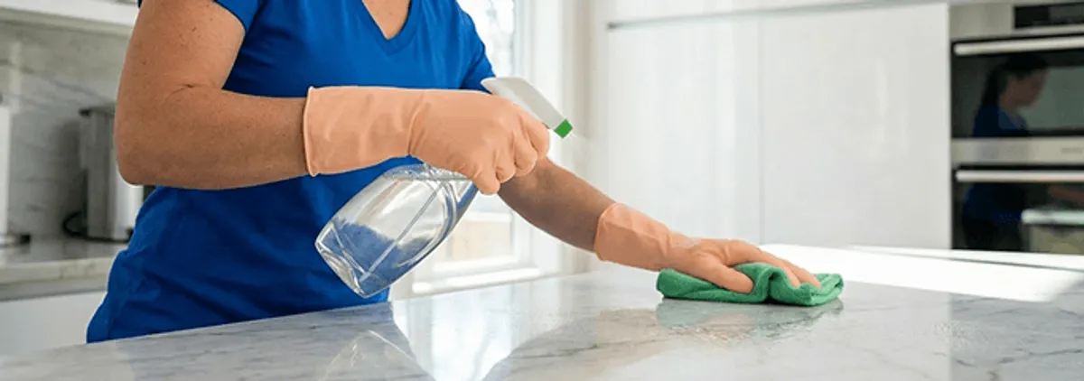 Maid service worker spraying and wiping a kitchen countertop with a microfiber cloth for sanitizing, Madison, WI.